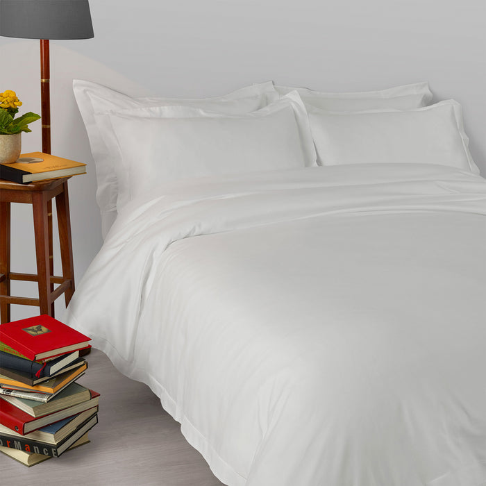 Suave-PaleGrey pillowcase and duvet cover on a bed with a lamp and books on a nightstand.