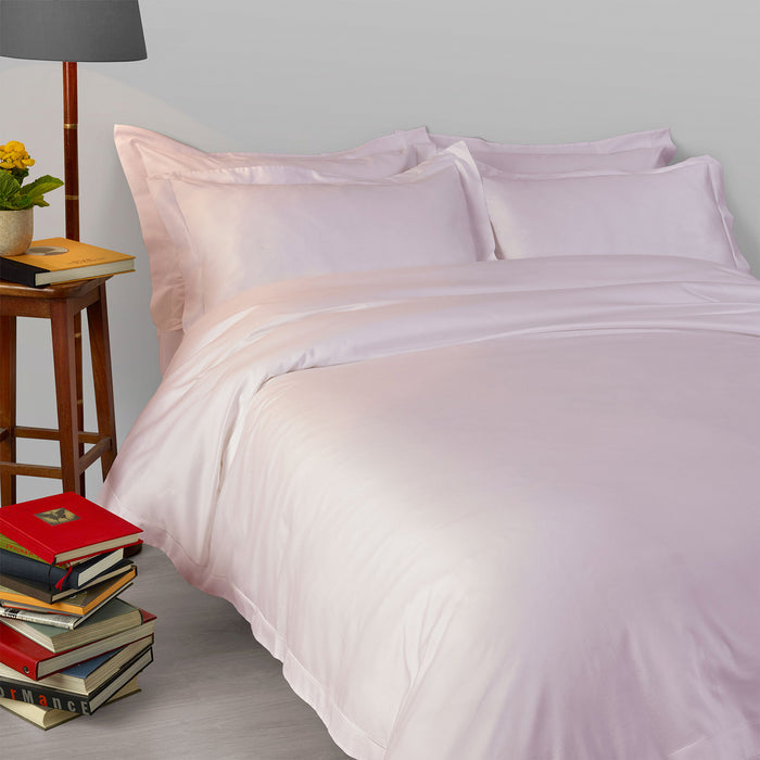 Neatly made bed with Suave-Pink-pillowcase and duvet cover, books, and a lamp in a bedroom setting.