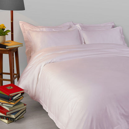 Neatly made bed with Suave-Pink-pillowcase and duvet cover, books, and a lamp in a bedroom setting.