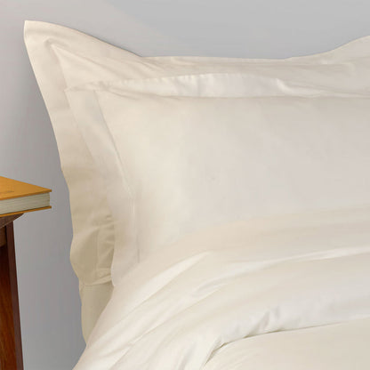 Close-up of Suave-Cream pillowcase and duvet cover on a bed with a wooden nightstand.