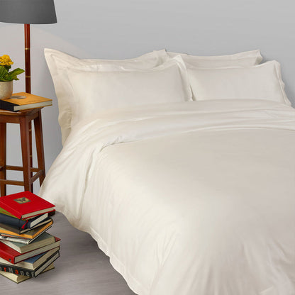 Suave-Cream pillowcase and duvet cover on a bed with books and a lamp in the background