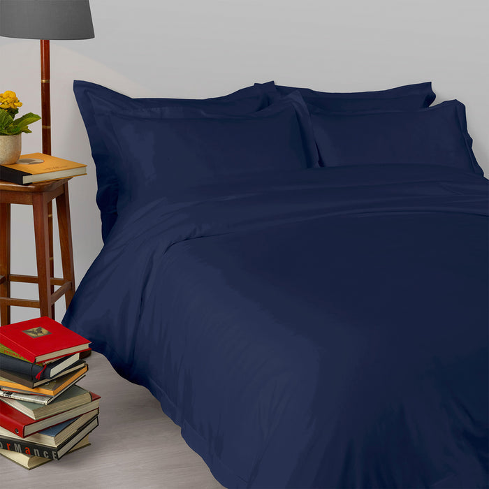 Suave-Midnight pillowcase and duvet cover on a bed with books and a lamp in the background.