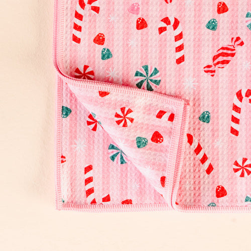 The Darling Effect Sugar Rush Waffle Tea Towel features a pink design with red and white candy canes, peppermints, and gumdrops. Both sides display the same festive pattern, with one corner folded to show the double-sided print.