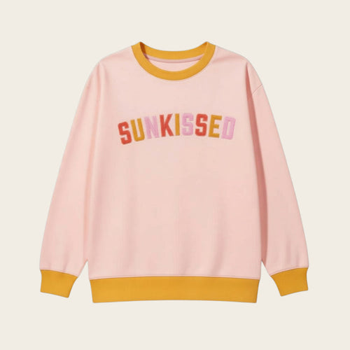 The Darling Effect’s Sunkissed Oversized Crew features a light pink shade with mustard yellow collar, cuffs, and hem. "SUNKISSED" is boldly printed in multicolored letters across the chest—a cozy piece for playful style.