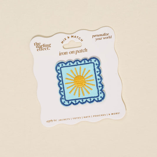 The Darling Effect's Sunshine Mix & Match Iron-On Patch features yellow rays on blue with a scalloped border, presented on a white card with gold text—perfect for customizing jackets or bags with a bright touch.