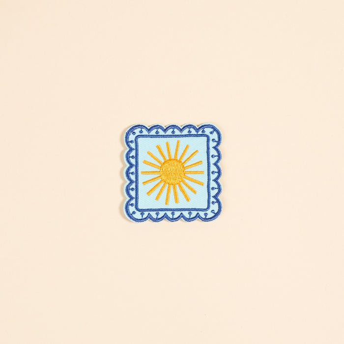 The Darling Effect’s Sunshine Mix & Match Iron-On Patch features a yellow sun with rays on light blue, bordered by blue scallops—a cheerful square accent for your patch collection.