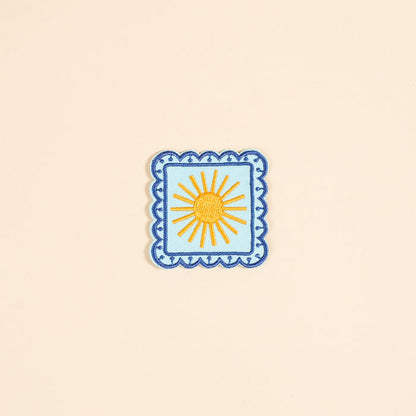 The Darling Effect’s Sunshine Mix & Match Iron-On Patch features a yellow sun with rays on light blue, bordered by blue scallops—a cheerful square accent for your patch collection.