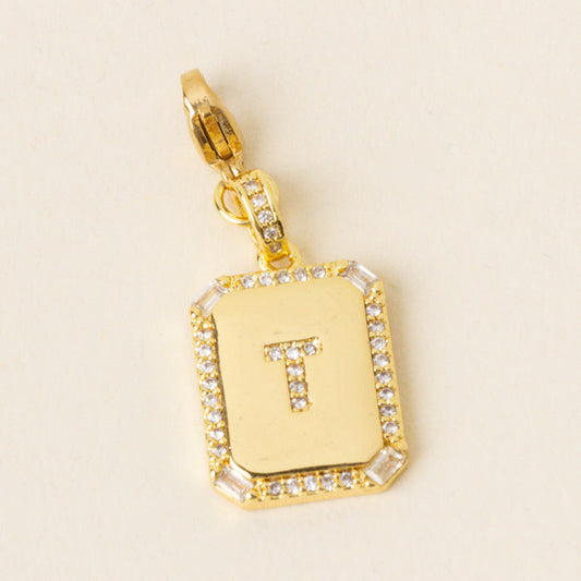 The-darling-effect T Jewelry Charm Initial Letter Gold features clear crystals on gold-plated brass, displayed on a beige background—ideal for personalized jewelry.