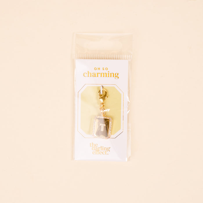 The-darling-effect T Jewelry Charm Initial Letter Gold: a gold-plated brass charm keychain featuring the letter T on gray, packaged on a white card with “OH SO charming” and “the darling effect” in a clear sleeve.