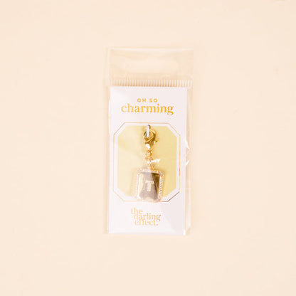 The-darling-effect T Jewelry Charm Initial Letter Gold: a gold-plated brass charm keychain featuring the letter T on gray, packaged on a white card with “OH SO charming” and “the darling effect” in a clear sleeve.