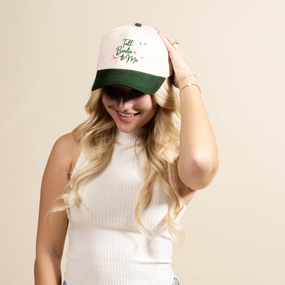 A woman with blonde hair smiles as she adjusts The Darling Effect's Talk Birdie to Me Classic Canvas Hat, cream and green with pink embroidery, highlighting her casual style.