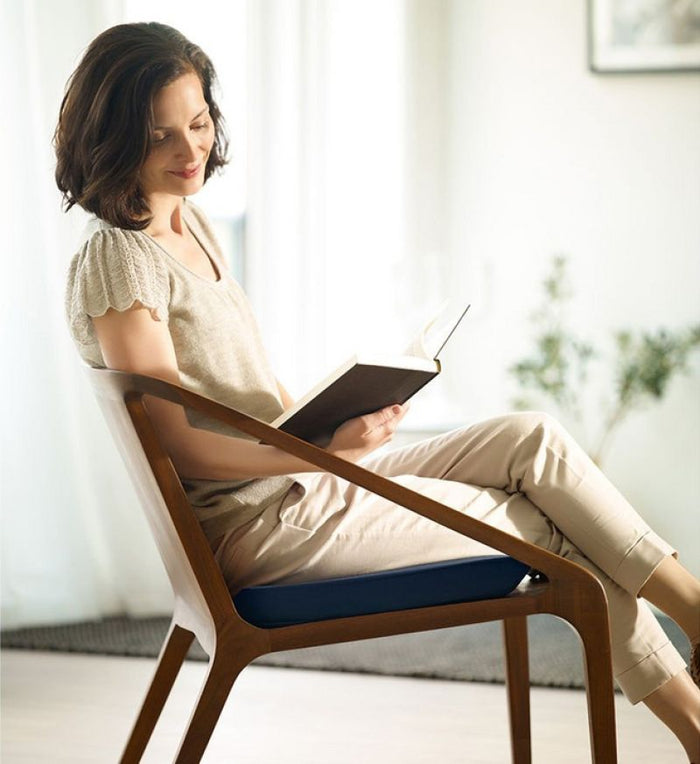 A woman reading a book while sitting on Tempur seat pad in a well lit room