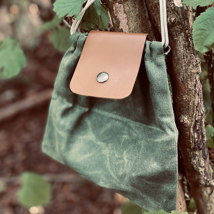 Forager Provisions LTD green up-cycled cotton canvas pouch with a vegan faux leather flap hanging on a tree branch.