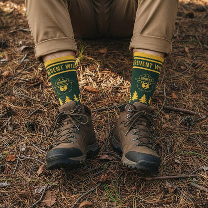 Wearing The Landmark Project Smokey Bear Emblem Sock - Pine, someone sits on a forest floor, outdoors adventure style.