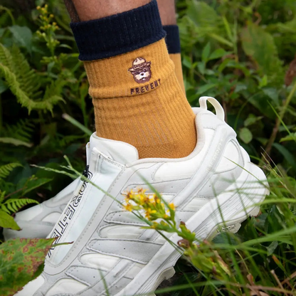 Forager Provisions LTD Smokey Bear message socks in mustard yellow with navy cuff worn with white hiking sneakers