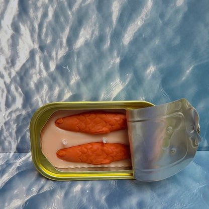 Forager Provisions LTD The Original Tinned Fish Candle with orange fish-shaped wax in a sardine-style tin on water background