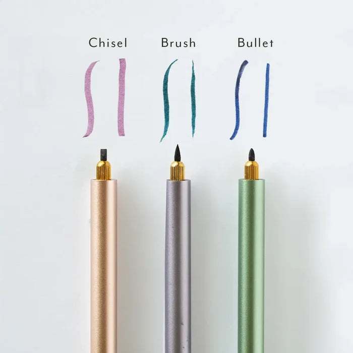 Three Tom’s Studio Lumos Creative Tip Set pens with interchangeable calligraphy tips, ink lines above each matching nib for artists.