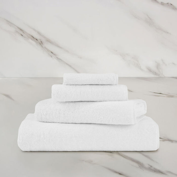 a white unito bath towel stacked on unito towels on a marbeled surface and background