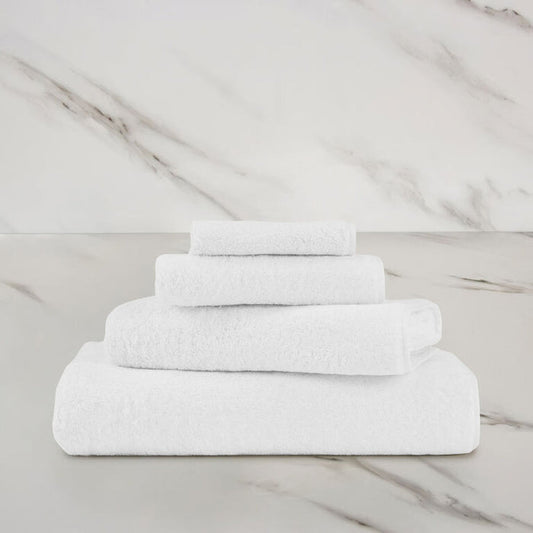 a white unito bath towel stacked on unito towels on a marbeled surface and background