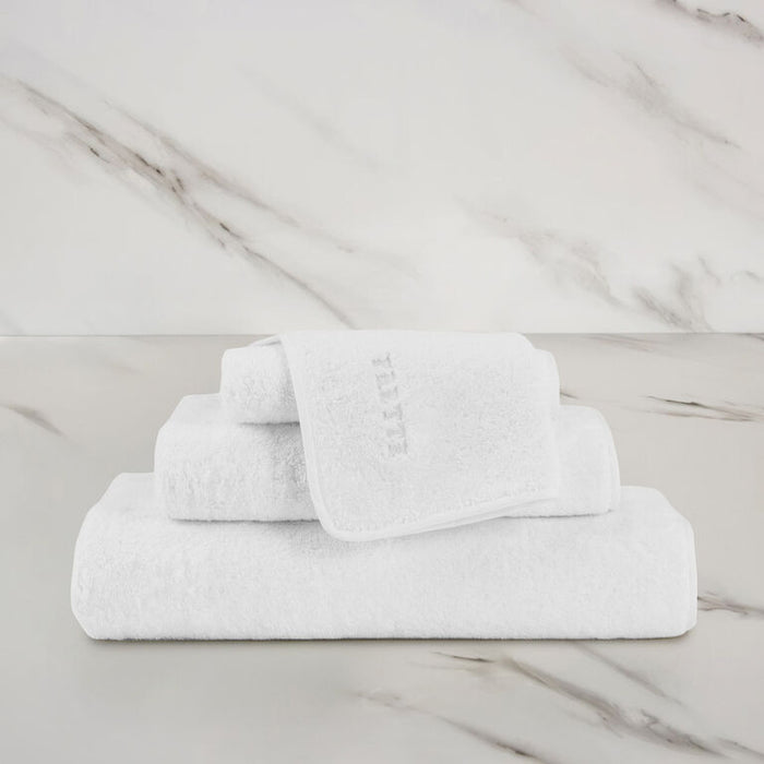 a white unito hand towel unfolded stacked on unito towels on a marbeled surface and background