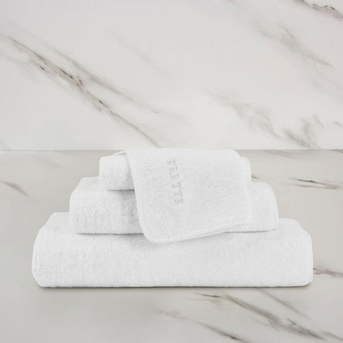 a white unito hand towel unfolded stacked on unito towels on a marbeled surface and background