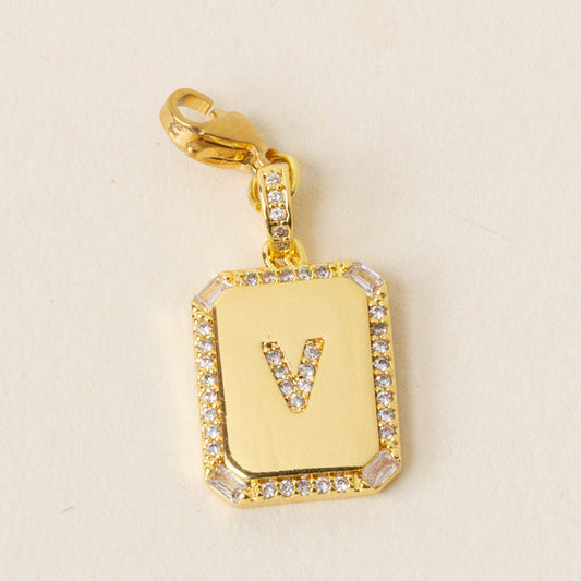 The-darling-effect's V Jewelry Charm Initial Letter Gold features a gold rectangular pendant with a center “V” engraving, clear gemstones along the border, and a gold clasp—ideal for personalized jewelry lovers.