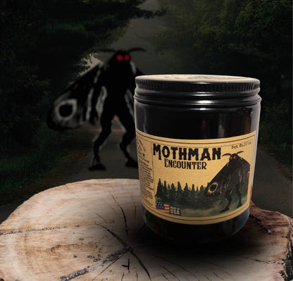 Forager Provisions LTD Mothman Encounter candle in a black jar with vintage-style label on a rustic wood slice.
