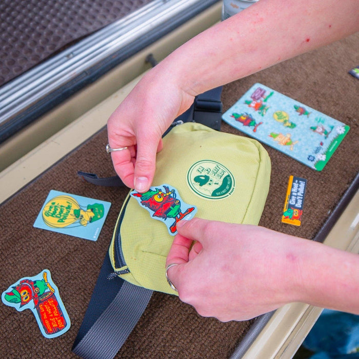 Attaching a Whistle Woodsy Owl NoSo Repair Patch to a yellow bag, with extra colorful NoSo patches nearby.