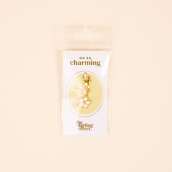 The-darling-effect White Flower Jewelry Charm Gold features a gold-tone charm with a white flower and yellow center, hanging from a clasp—ideal for your charm bar. It comes on an "OH SO charming" card.