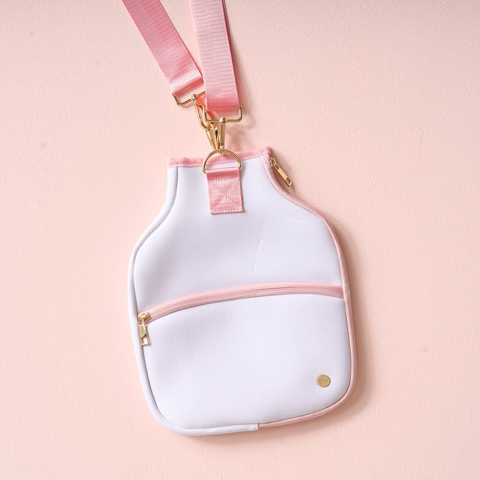 The Darling Effect’s White Pickleball Paddle Case features a light pink and white design, gold hardware, an adjustable pink strap, and a zippered front pocket—ideal for essentials or your paddle—shown on a pale pink background.