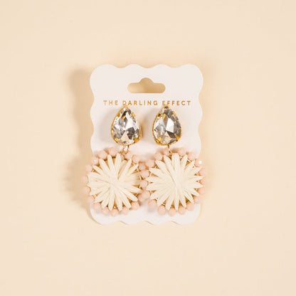 White Radiant Gem Earrings by The Darling Effect feature a raffia sunburst design with pink beads, presented on a branded card—perfect lightweight earrings for everyday wear.