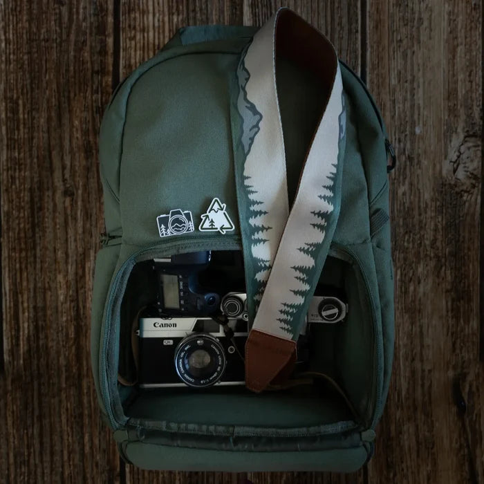 Green backpack with decorative pins, open pocket showing Canon camera and Wildtree Landscape Camera Strap. Perfect for travel.