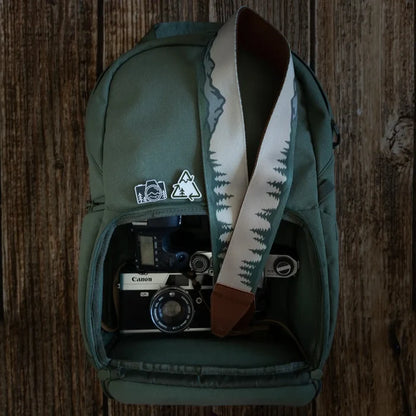 Green backpack with decorative pins, open pocket showing Canon camera and Wildtree Landscape Camera Strap. Perfect for travel.
