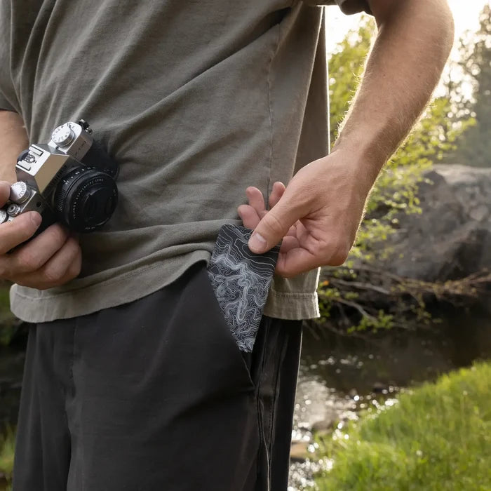 By the water outdoors, person holds camera and pockets Wildtree Topographic Map SD/Switch Card Holder for adventure storage.