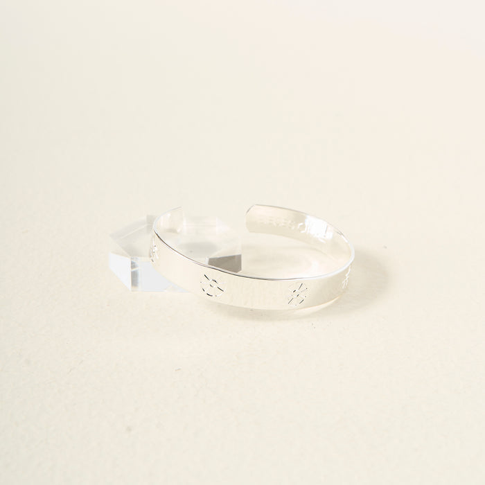 The Darling Effect’s You Are Outgoing Cuff Bracelet, crafted in sterling silver with cut-out floral designs, is displayed on a clear acrylic stand against a light cream background—a thoughtful gift for someone special.
