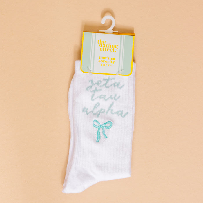 Show your sorority spirit with Zeta Tau Alpha Embroidered Crew Socks by The Darling Effect, featuring light blue lettering and a bow, packaged with a branded tag.