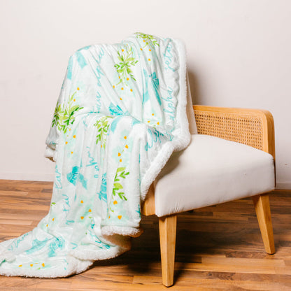 The Darling Effect’s Zeta Tau Alpha Plush Sherpa Blanket features a white and mint green floral design with teal bows—ideal for sorority life or as a cozy college dorm throw, draped stylishly over any modern accent chair.